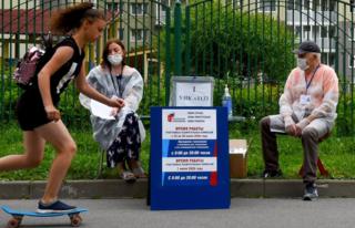 A girl skates her board past members of a local electoral commission wearing face masks