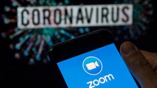 Zoom logo seen displayed on a smartphone with a computer model of the COVID-19 coronavirus on the background.