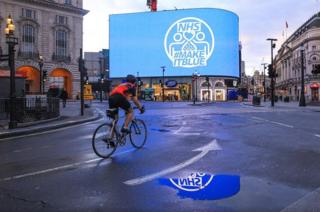 Cyclist in empty Piccadilly Circus with large NHS billboard