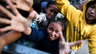 Earthquake survivors scuffle to receive food being distributed from a police truck outside a makeshift camp in Palu, Indonesia, on October 2, 2018
