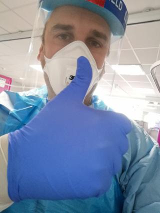 An NHS worker in PPE shows a thumbs up to the camera