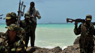 Armed militiamen and a pirate walk on a rocky outcrop on the coast in the central Somali