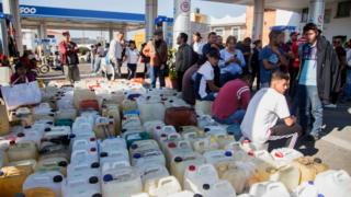 Personas sentadas frente a una gasolinera.
