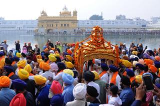 Sikh devotees carrying the Sri Guru Granth Sahib ji - the holy book of Sikh religion - in a hand-held, golden carriage