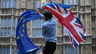 Мужчина держит Юнион Джек и флаг ЕС возле здания парламента