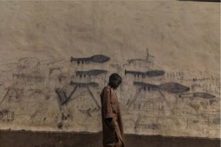 A child stands in front of wall covered in drawings
