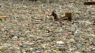 A scavenger wades through garbage in Manila, 2016