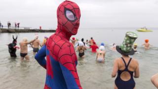 A person dressed in a Spiderman costume and others walk into Lake Geneva
