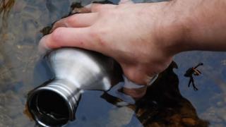 Una persona recogiendo agua con un termo en un pozo