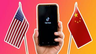 Between two flags - one US and one China - a hand holds up a phone with the TikTok logo on it