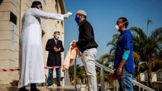 A man carrying a prayer mat and wearing a mask as preventive measure against COVID-19 coronavirus has his temperature checked at the entrance of the Nizamiye Mosque ahead of the Friday prayer in Midrand, Johannesburg, on June 5, 2020