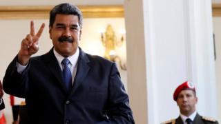 Venezuela's President Nicolas Maduro smiles to the media after a meeting, with a military officer visible nearby behind him