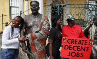Members of South Africa's trade union take a break from their May Day march to push for better wages to pose with statues in Cape Town on 1 May 2018