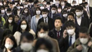 Офисные работники в защитных масках, чтобы избежать заражения от коронавируса, идут к своим офисам после переполненных пригородных поездов на железнодорожной станции в центре Токио, Япония, 6 апреля 2020 г.