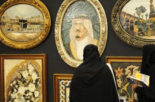 امرأة سعودية تنظر إلى لوحة للملك السعودي