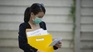 Woman in mask clutches folder saying 'layoff'