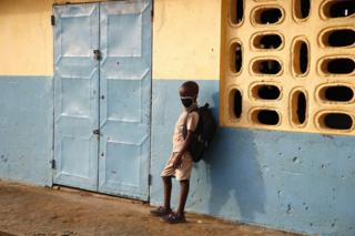 A student wearing a face mask stands outside a classroom.