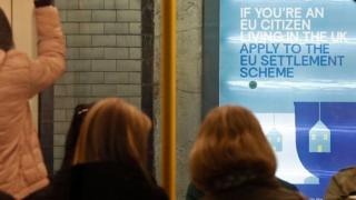 A poster encouraging EU nationals to apply to the government's post-Brexit EU settlement scheme is pictured through a carriage of a London Underground tube train