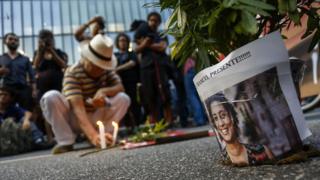 Foto de Marielle Franco ao lado de pessoas que acendem velas e prestam homenagem à vereadora