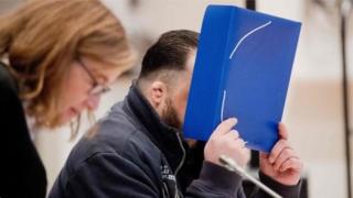 Нільс Хегель ховає своє обличчя за папкою