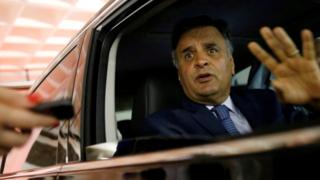 Aécio Neves acena de dentro de carro, com olhar levemente tenso