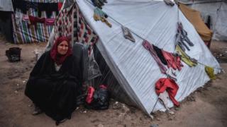 A woman sits next to a makeshift tent in Rafah, Gaza