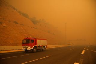 Fire fighters are seen amid smoke as a wildfire burns in Kineta, near Athens.