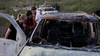 Relatives of slain members of Mexican-American families belonging to Mormon communities observe the burnt wreckage of a vehicle where some of their relatives died