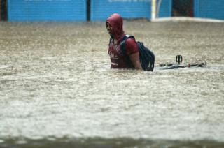 An young man pulls his bicycle through a flooded street during heavy rain showers in Mumbai on 29 August 2017.