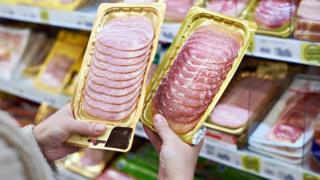 Mujer con bandejas de jamón en las manos.