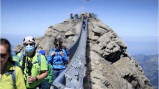 Tourists wearing protective face masks walk on the Peak Walk suspension bridge of Glacier 3000, in Les Diablerets, Switzerland