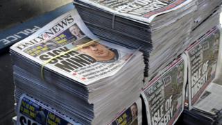 Stacks of Daily News and New York Post tabloid newspapers sit on a sidewalk in New York, New York.