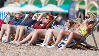 A group of women sat in the sun on a beach in Brighton, Britain