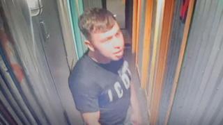 CCTV image of a man in his late teens or early 20s, about 5ft 10ins, of medium build, with medium-length brown hair which was shaved on the side and longer on the top. He is wearing blue jeans and a black t-shirt.