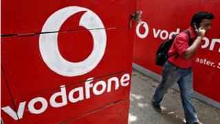 A man speaks on his mobile phone as he walks past logos of Vodafone painted on a roadside wall in Kolkata May 20, 2014