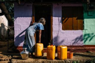 A woman collects water in containers outside her house