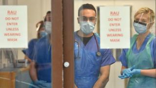 Медицинский персонал в средствах индивидуальной защиты (СИЗ) ожидает приема пациентов с коронавирусом у дверей отделения респираторной оценки в больнице Морристон в Суонси