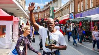 A man holds his arm up as he preaches in a busy street