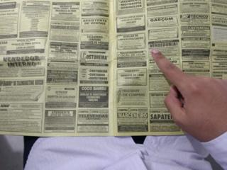 Imagem mostra mão apontando para vaga de emprego nos classificados do jornal