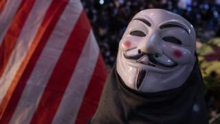 An Anonymous mask is seen next to a US flag in this photograph, which was actually taken in Hong Kong during the pro-democracy protest there in 2019