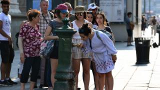 People queue to drink water from a public tap near the Duomo Cathedral, in Milan