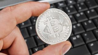 Man's hand holding 'bitcoin' over laptop keyboard