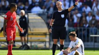 Un árbitro regaña a un jugador peruano mientras uno neozelandés está en el suelo