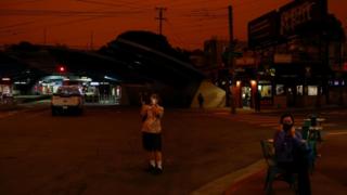 A pedestrian takes a photo of an orange sky darkened by smoke from California wildfires