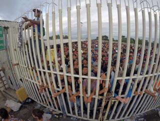 Honduran migrants wait behind a gate after crossing the fence on the border with Guatemala to enter Mexico