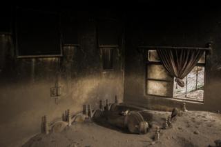 A damaged room in a house covered in ash