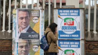 A woman walks past electoral posters of the 5 Star"s candidate Luigi Di Maio and the Forza Italia party in Pomigliano D'Arco, near Naples, Italy, February 21, 2018