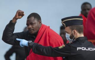 Un inmigrante de raza negra alza el puño mientras es custodiado por un policía español