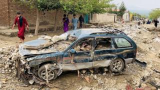 An Afghan man walks past a damaged car after floods in Charikar
