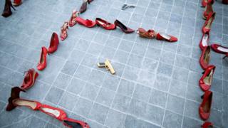 Pairs of women's red shoes are displayed next to a toy gun during the 